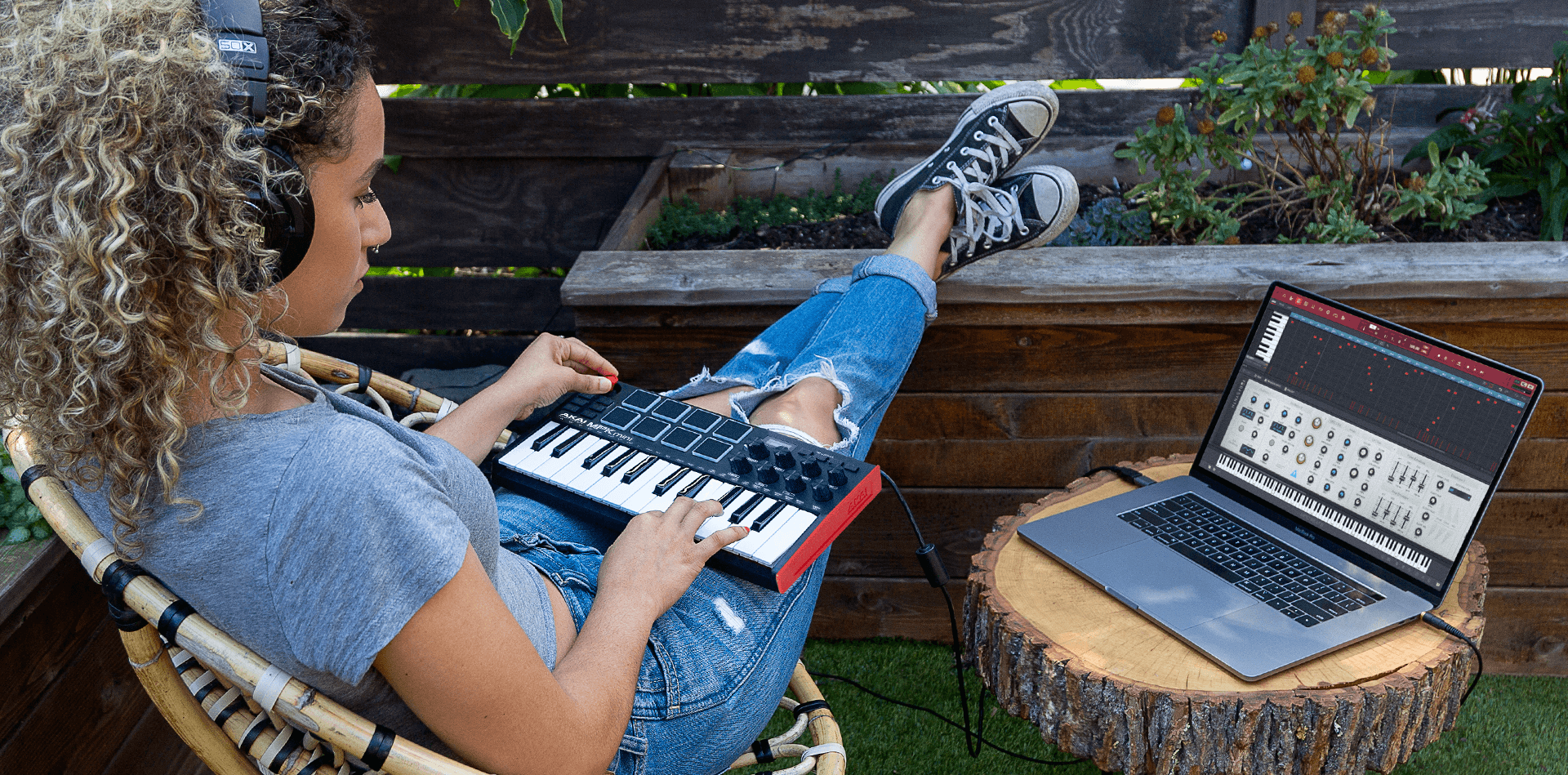 A woman making beats outside on her laptop while playing a MIDI piano