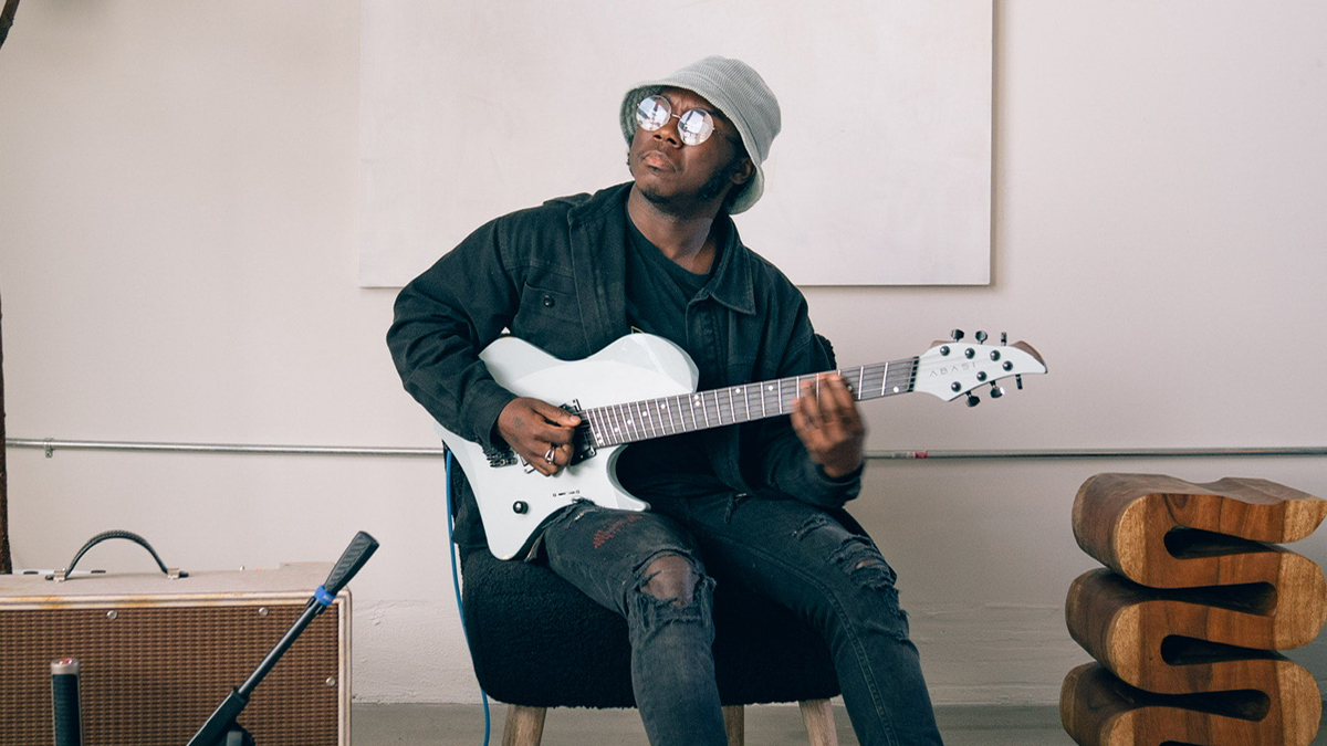 A music producer in a bucket hat playing a white electric guitar in a bright studio.