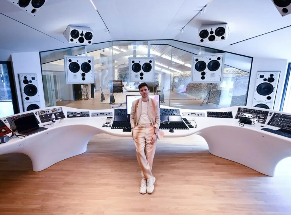 Professional music producer standing in a futuristic white recording studio with high-end monitors and mixing console.